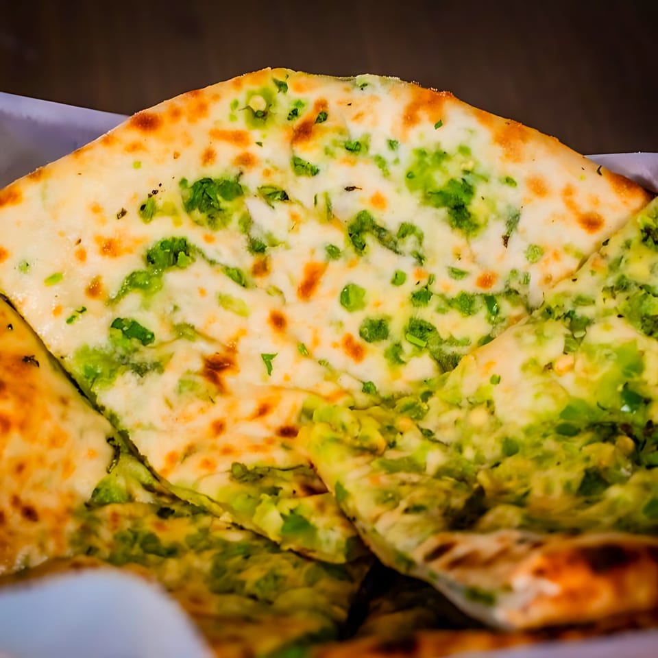 Close-up of garlic naan bread, golden brown with green herbs, from Jannat Indian Restaurant.
