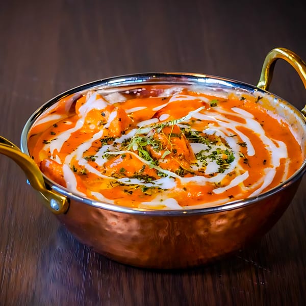 Jannat Indian Restaurant's vibrant orange curry, drizzled with cream and fresh herbs in a copper pot.