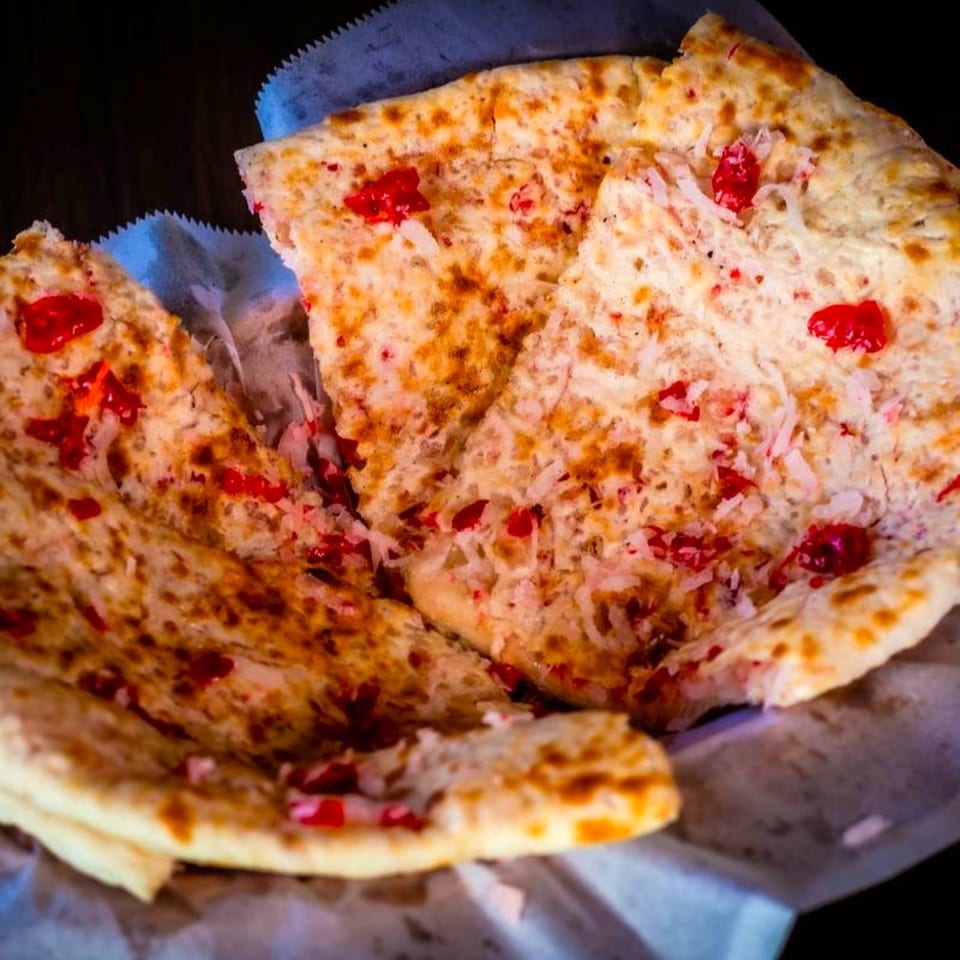 Sweet naan bread, topped with red cherries and shredded coconut, served in a basket.