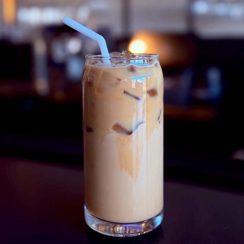 Iced coffee with a light blue straw in a tall glass, on a dark surface.