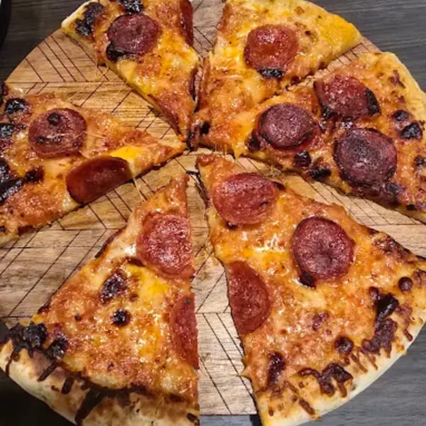Pepperoni pizza cut into slices on a wooden board, with melted cheese and charred edges.