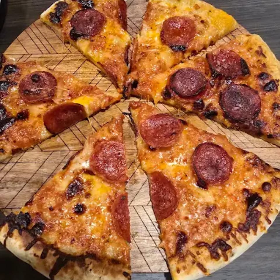 Pepperoni pizza cut into slices on a wooden board, with melted cheese and charred edges.