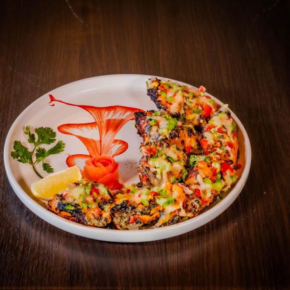 Indian grilled chicken with melted cheese, colorful peppers, cilantro, and lemon on a white plate.