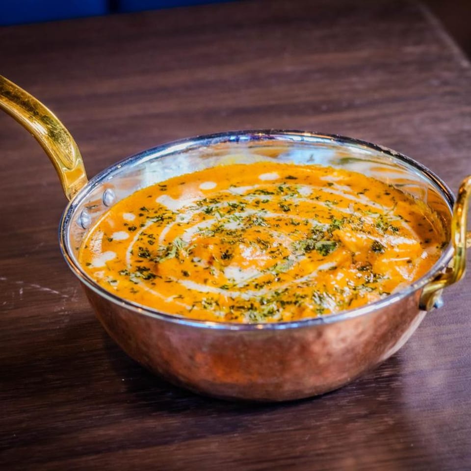 Jannat Indian Restaurant's creamy orange curry with white swirls and green herbs in a copper pot.