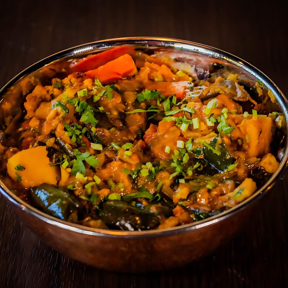 A close-up of a vibrant Indian curry with vegetables and herbs in a metal bowl.